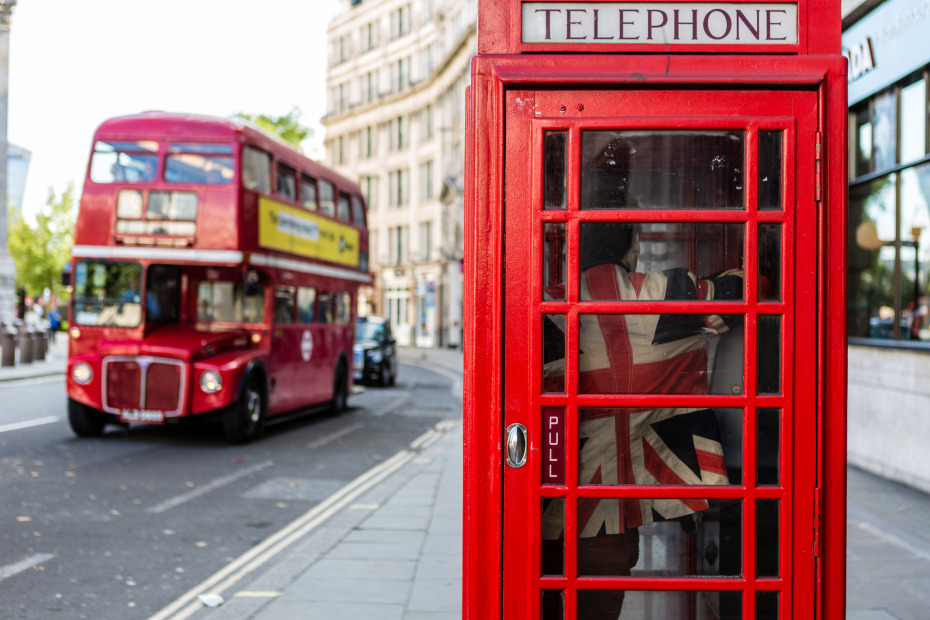 A brit guy in a brit phone booth with a brit bus.